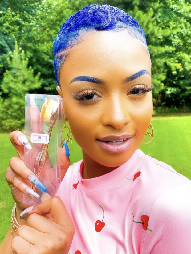 Woman holding makeup brushes with a green outdoor background