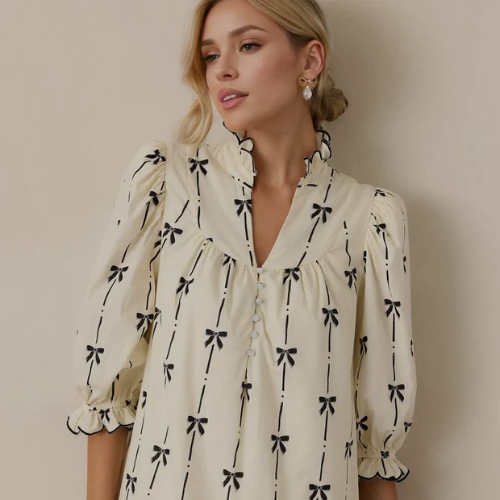 Woman wearing a cream blouse with black bow pattern against a plain background