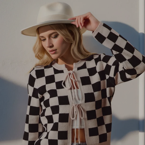 Woman wearing a black and white checkered sweater with a white hat against a light background
