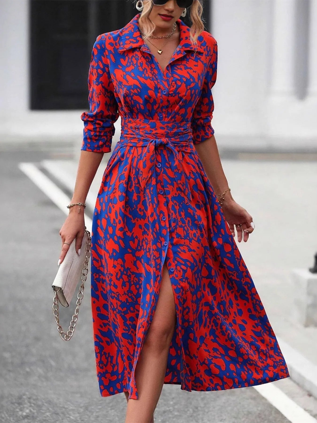 Woman wearing a red and blue patterned dress with a belt, standing on a street.