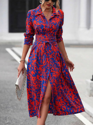 Woman wearing a red and blue patterned dress with a belt, standing on a street.